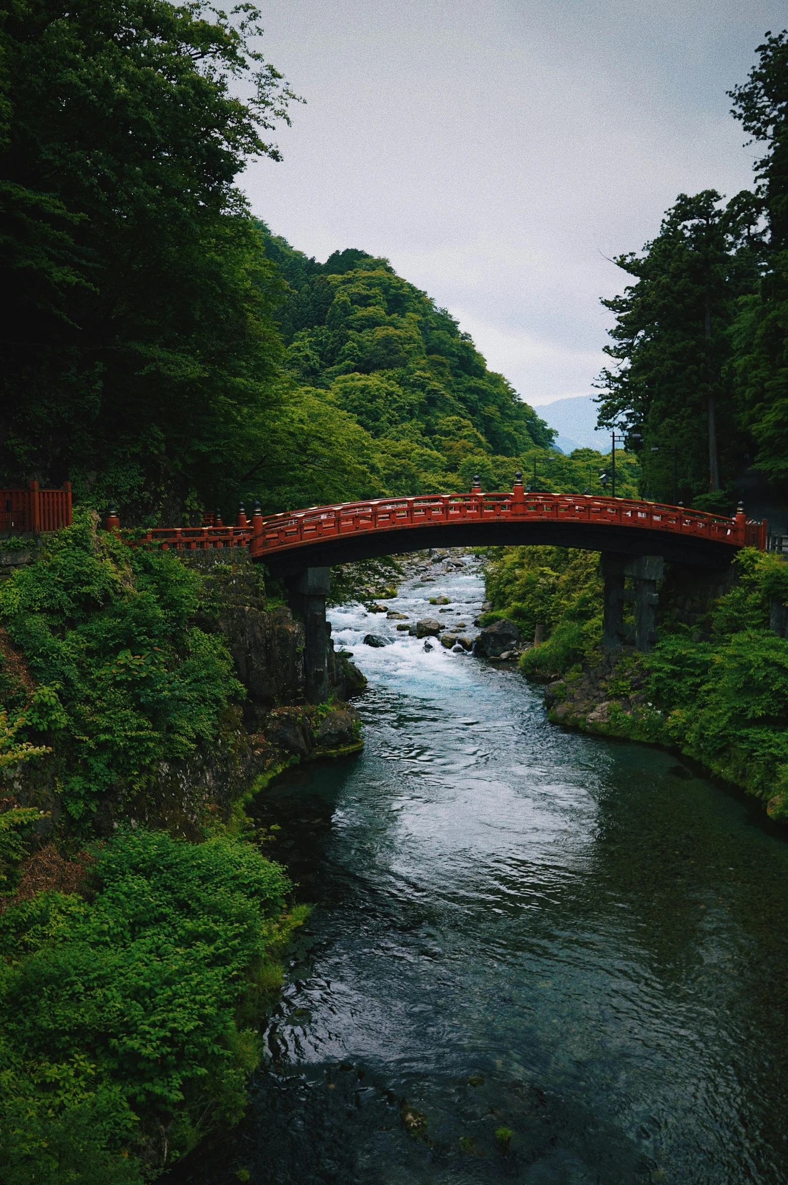 a red bridge over a river surrounded by trees, pexels contest winner, ukiyo-e, slight overcast lighting, valley, vacation photo, green waters