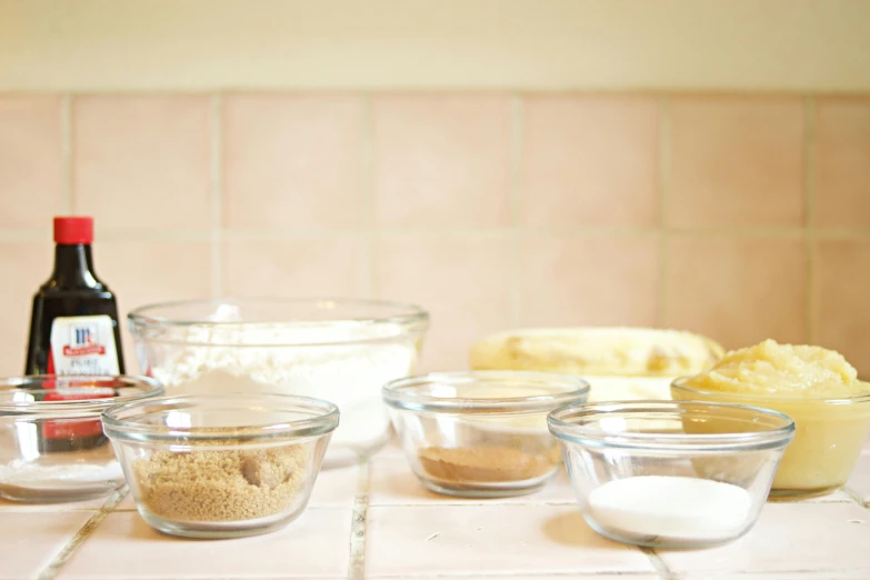 a counter topped with bowls of food next to a bottle of wine, by Lucette Barker, process art, baking cookies, beakers, thumbnail, white