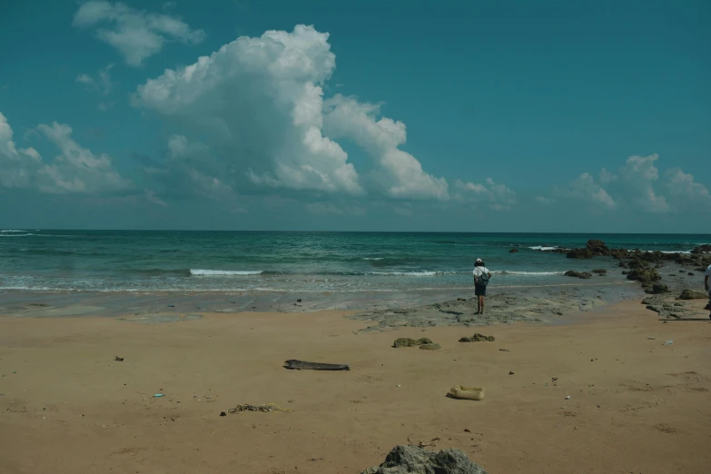 a man standing on top of a sandy beach next to the ocean, nivanh chanthara, cinematic still frame, **cinematic, 5 feet away