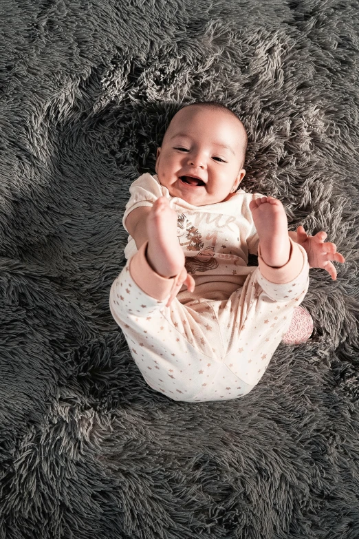 a baby sitting on top of a gray rug, inspired by Margaret Geddes, pexels contest winner, smiling down from above, full colour, lulu chen, soft and fluffy