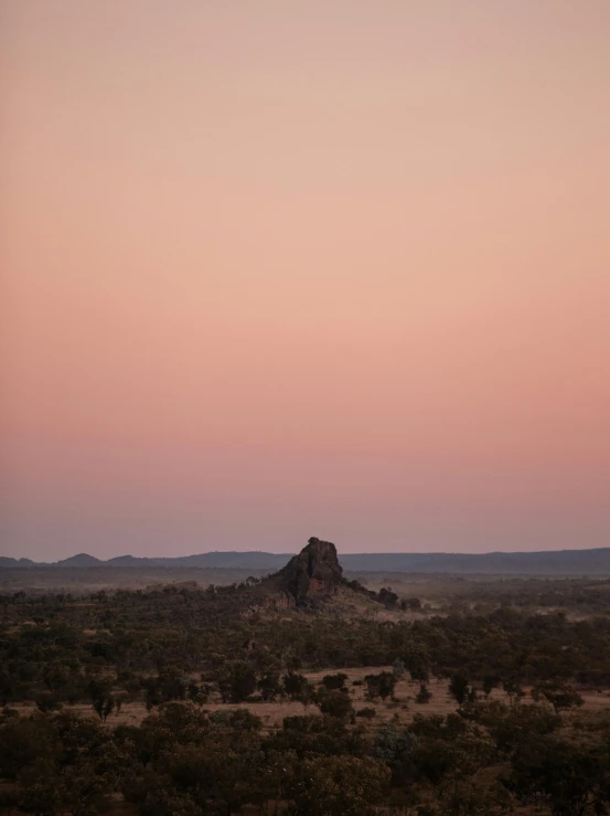 a large rock in the middle of a desert, by Lee Loughridge, unsplash contest winner, australian tonalism, pink skies, from the distance, castle in the distance, break of dawn on pluto