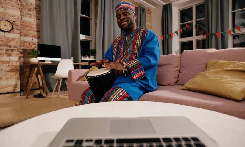 a man sitting on a couch in front of a laptop, inspired by Ras Akyem, pexels contest winner, afrofuturism, playing drums, wearing festive clothing, islamic, congas