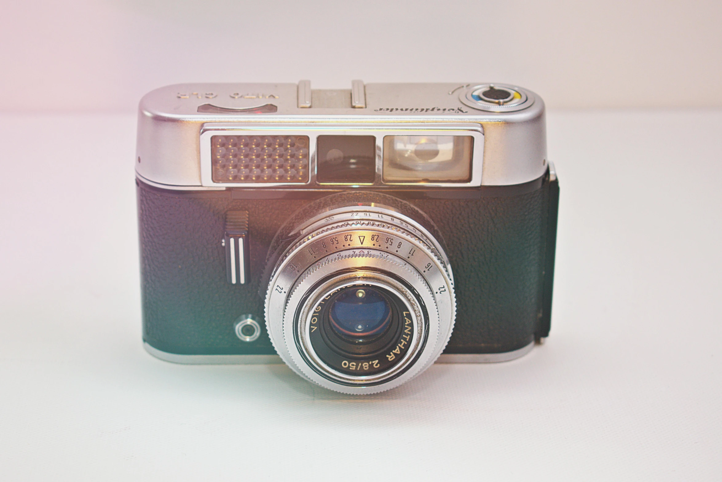 a close up of a camera on a table, by Sven Erixson, unsplash, photorealism, 1960s technicolor, silver, on a pale background, bright camera flash