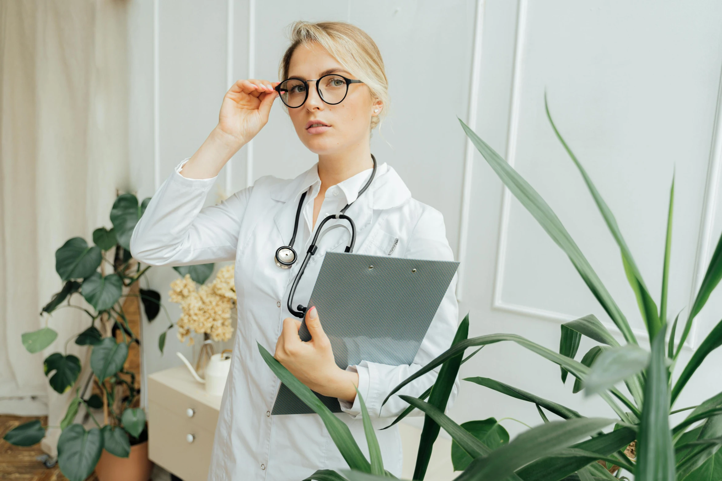 a woman with a stethoscope standing next to a potted plant, pexels contest winner, wearing black rimmed glasses, doctors office, anastasia ovchinnikova, looking around a corner