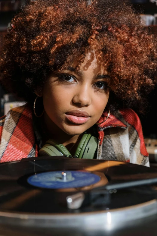 a close up of a person with a record on a table, an album cover, trending on pexels, funk art, mixed race woman, djing with dj turntables, curly copper colored hair, teenage girl