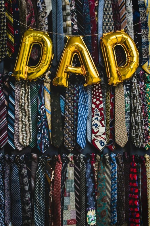 a wall filled with lots of different types of ties, trending on unsplash, dada, party balloons, i'm dad, gold clothes, detailed letters