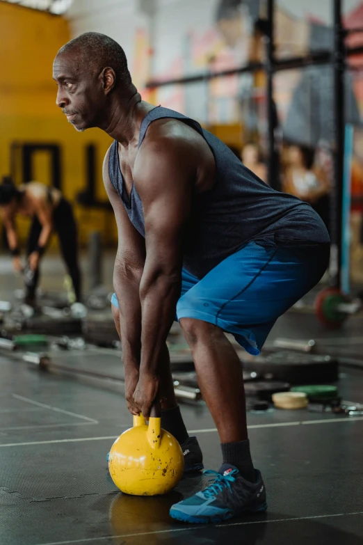 a man holding a yellow kettlebell in a gym, by Dan Luvisi, pexels contest winner, figuration libre, instagram story, emmanuel shiru, center focused, lower back