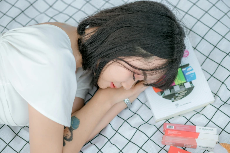 a woman laying on top of a bed next to a pile of books, pexels contest winner, blunt bangs fall on her forehead, profile image, asian female, broken down