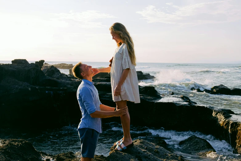 a man standing on top of a rock next to a woman, pexels contest winner, happening, man proposing his girlfriend, coastal, alana fletcher, youtube thumbnail