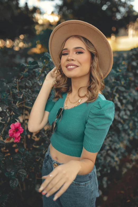 a woman wearing a hat standing in front of a bush, by Robbie Trevino, instagram, wearing a cropped tops, wearing a green sweater, smiling down from above, profile image