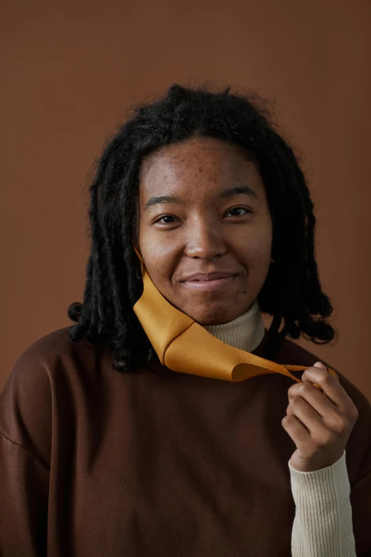 a woman wearing a brown sweater and a yellow tie, trending on unsplash, light brown skin, nonbinary model, ribbon, sza