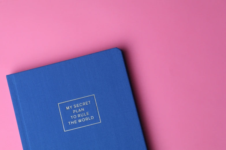 a blue book sitting on top of a pink surface, golden rule, secrets, the world, product photograph