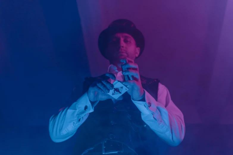 a man standing in front of a purple and blue light, an album cover, inspired by Edmond Bille, unsplash, renaissance, suit vest and top hat and gloves, performing a music video, dimly lit scene, the card player man