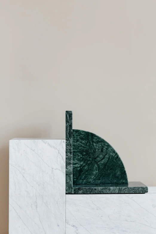 a marble bookend sitting on top of a shelf, by Emma Andijewska, unsplash, de stijl, forest green, white sweeping arches, half moon, right side composition