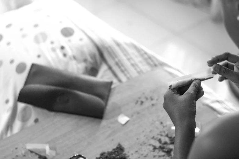 a black and white photo of a person sitting at a table, process art, ganja, clay amulets, laying down, joints