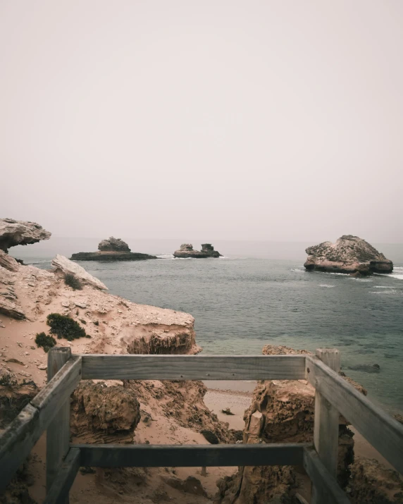 a bench sitting on top of a sandy beach next to the ocean, rock arches, instagram picture, balcony, an ominous haze