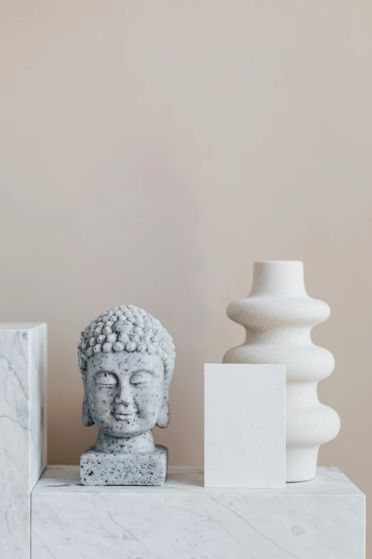 a white vase sitting on top of a shelf next to a buddha statue, a marble sculpture, trending on pexels, minimalism, square face, stone statues, mixed materials, design on a white background