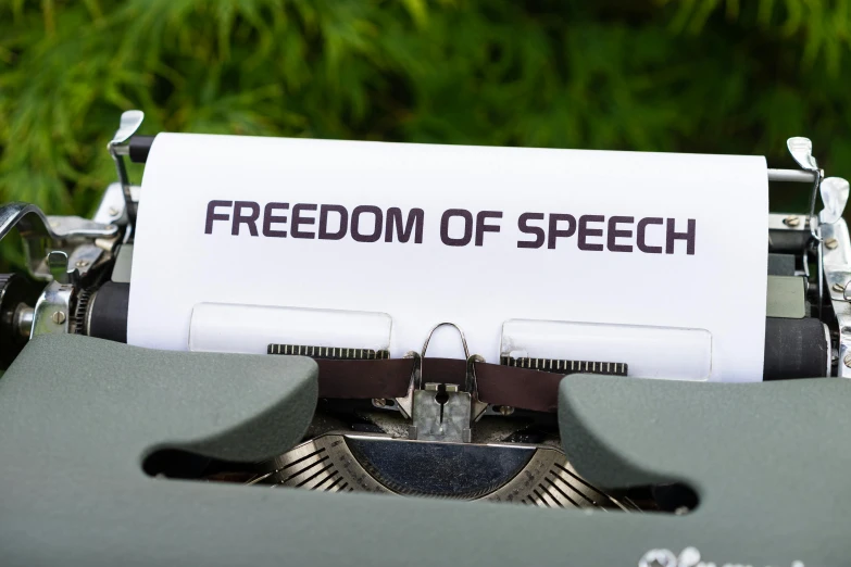 a typewriter with a paper that reads freedom of speech, by Niko Henrichon, shutterstock, serene environment, seen from below, emma uber, patriotism