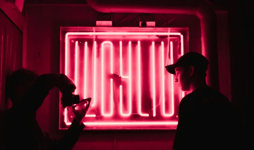 two people standing in front of a neon sign, by Mathias Kollros, unsplash contest winner, realism, neon pink and black color scheme, red light from some windows, selfie, liquid light