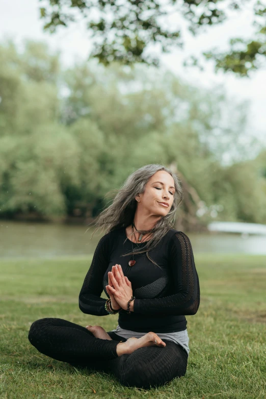 a woman sitting in the grass doing yoga, long grey hair, with a tree in the background, lena oxton, high-quality photo
