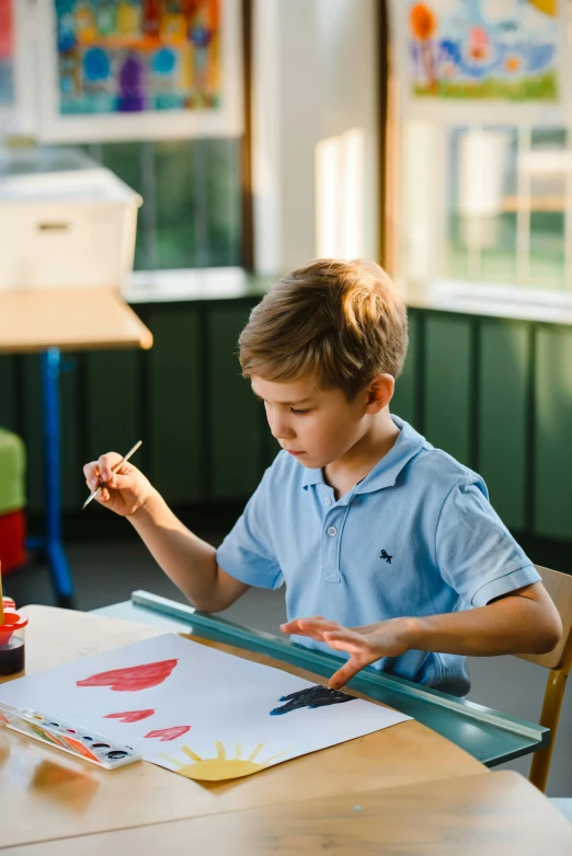 a little boy that is sitting at a table, inspired by Kyffin Williams, pexels contest winner, process art, beautiful daylight, private school, holding a paintbrush, colorful scene