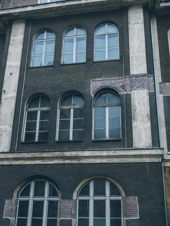 a motorcycle parked in front of a tall building, inspired by Lajos Gulácsy, pexels contest winner, berlin secession, dull flaking paint, black windows, before a stucco wall, charcoal and silver color scheme