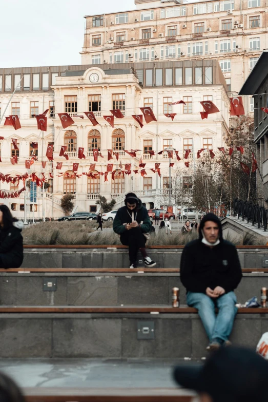 a group of people sitting on a bench in front of a building, red flags, in the middle of the city, istanbul, light academia aesthetic