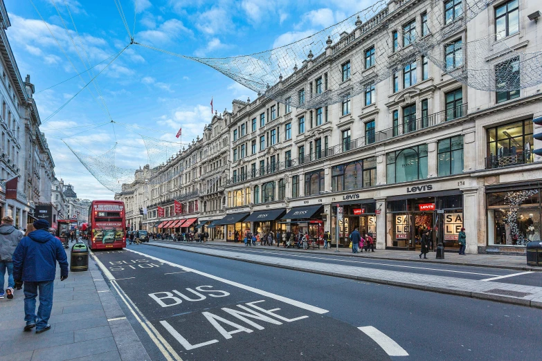 a group of people walking down a street next to tall buildings, london bus, lots of shops, neo classical architecture, profile image