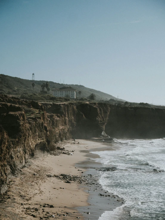 a man riding a surfboard on top of a sandy beach, by Kristin Nelson, pexels contest winner, coastal cliffs, erosion algorithm landscape, beachfront mansion, with a long