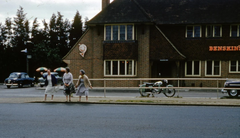 a group of people standing on the side of a road, 1 9 6 0 s cafe racer, esher, seen from far away, tudor