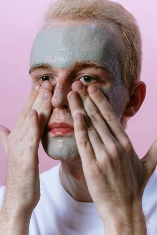 a man with a face mask covering his eyes, by Jessie Alexandra Dick, aestheticism, pastel pink skin tone, promo image, shaven, hand on his cheek