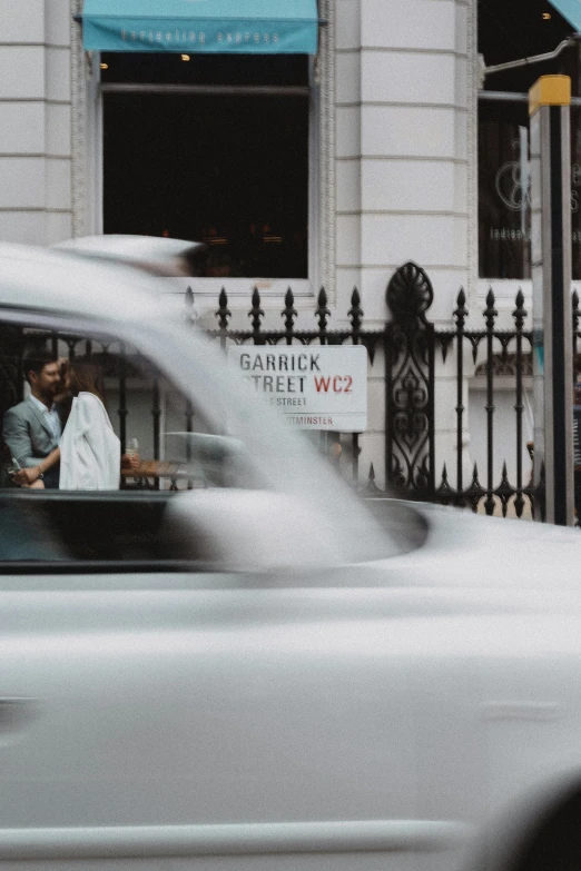 a white car driving down a street next to a tall building, by Daniel Seghers, pexels contest winner, couple kissing, speeding through london, ignant, gif