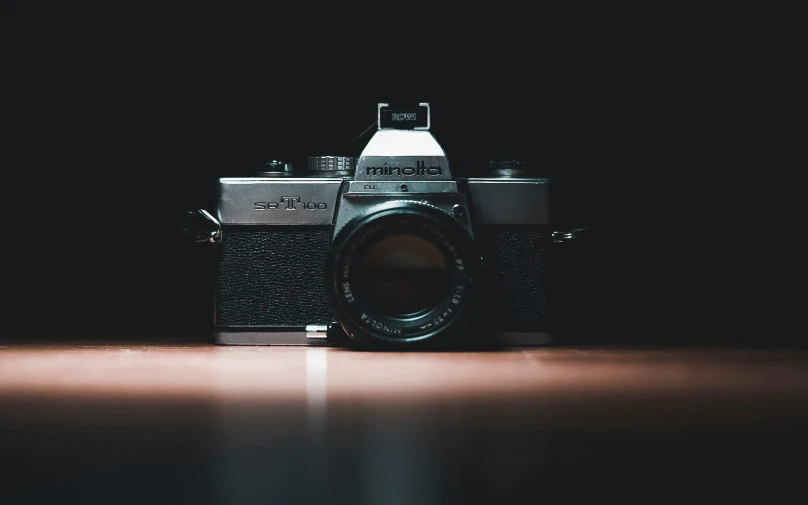 a camera sitting on top of a wooden table, by Niko Henrichon, unsplash contest winner, medium format. soft light, 80s photo, dark photograph, looking into camera