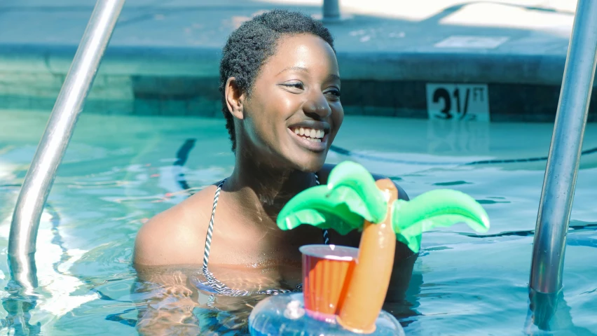 a woman holding a plastic palm tree in a pool, by Lily Delissa Joseph, pexels contest winner, brown skinned, holding a drink, serene smile, float