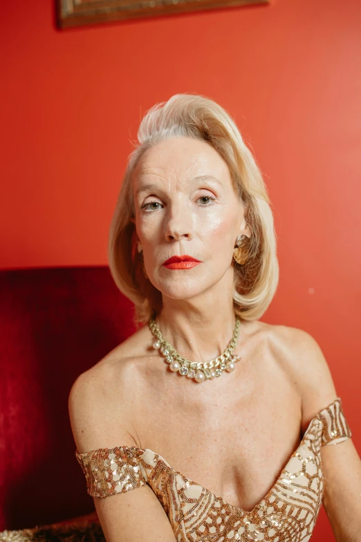 a woman in a gold dress sitting on a red couch, inspired by Jean Cunningham, trending on pexels, pointé pose;pursed lips, 7 0 years old, die antwoord, covered in jewels