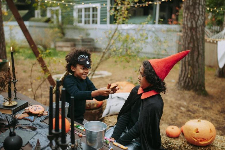a couple of people that are sitting at a table, pexels contest winner, black witch hat and broomstick, kids playing, square, outdoor photo