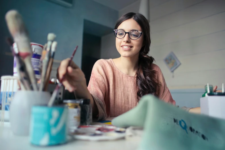 a woman sitting at a table with paint brushes, pexels contest winner, with glasses on, student, pokimane, mate painting