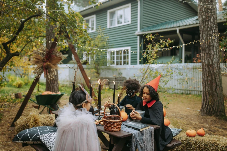 a group of people sitting around a table, by Liza Donnelly, pexels contest winner, witch hut, costumes, outdoor, birthday party