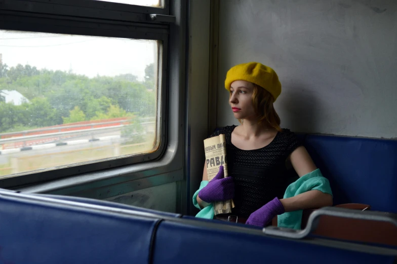 a woman sitting on a train looking out a window, a portrait, regionalism, yellow latex gloves, wearing a french beret, ukraine. photography, square