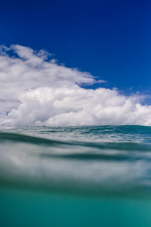 a man riding a wave on top of a surfboard, by Peter Churcher, unsplash, clouds on surface, kauai, extreme panoramic, today\'s featured photograph 4k