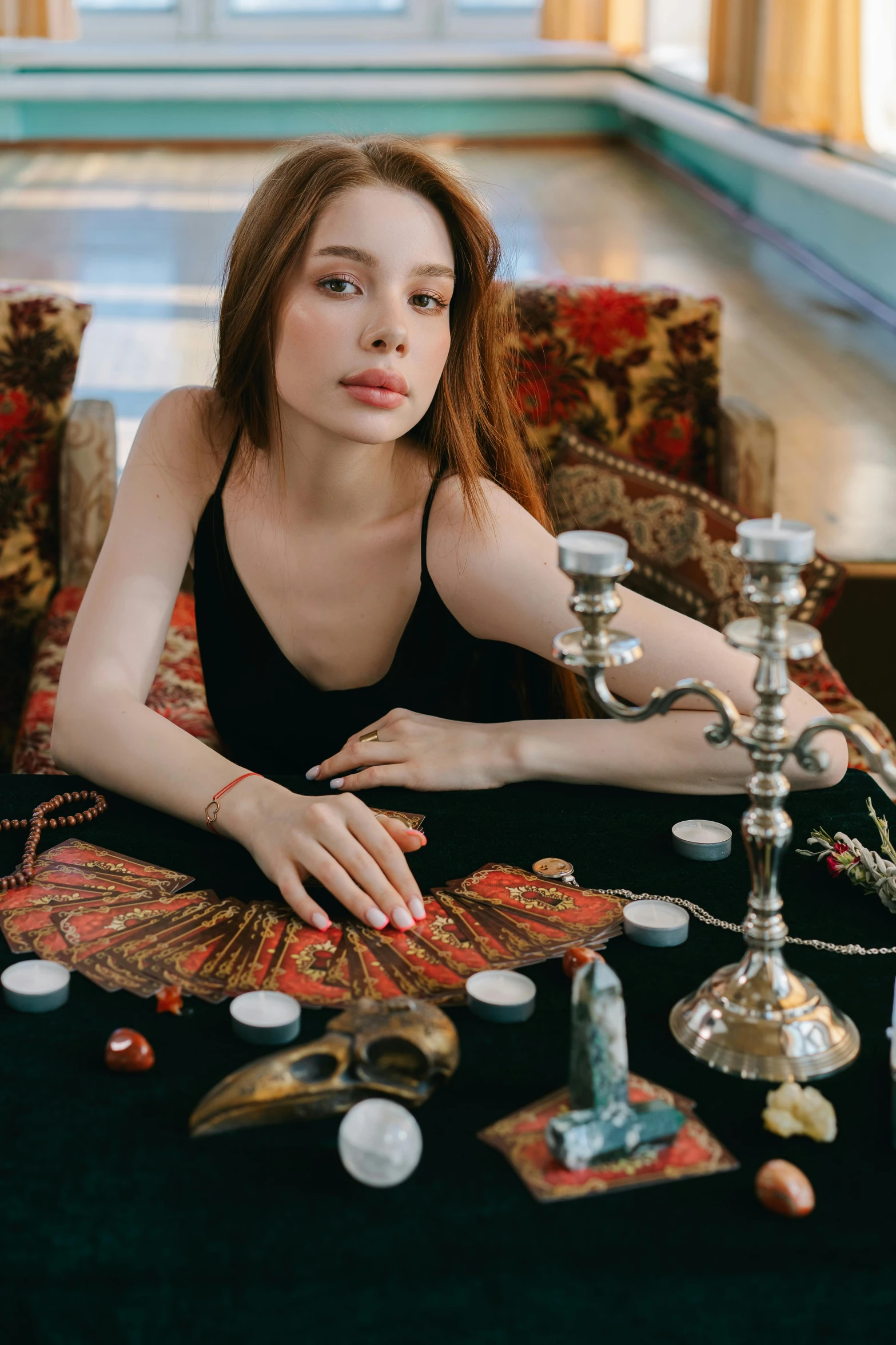 a woman sitting at a table with candles, a portrait, by Julia Pishtar, trending on pexels, black and red silk clothing, a pale skin, wearing psychedelic wicca, sitting on a mocha-colored table