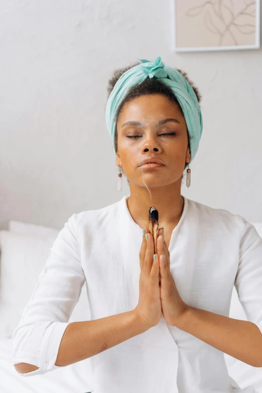 a woman sitting in a meditation position on a bed, trending on pexels, renaissance, cloth head wrap, praying with tobacco, pastels, hands on face