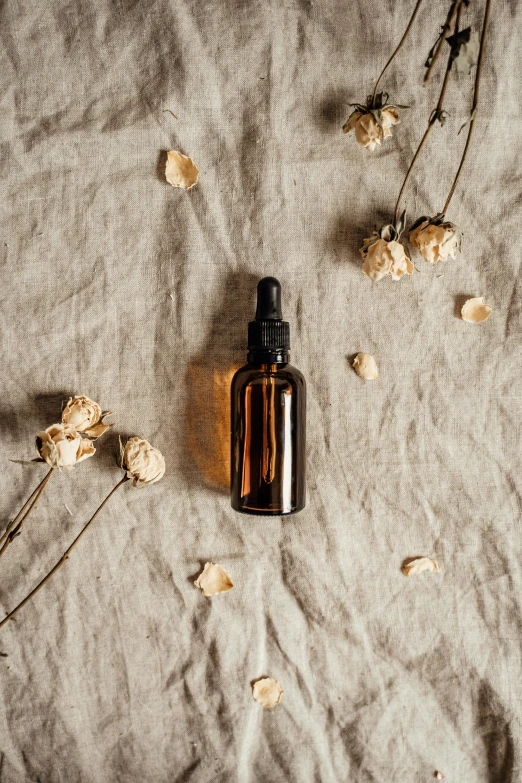 a bottle of essential oil next to dried flowers, by Andries Stock, trending on pexels, linen canvas, thumbnail, brown, made of wax and oil