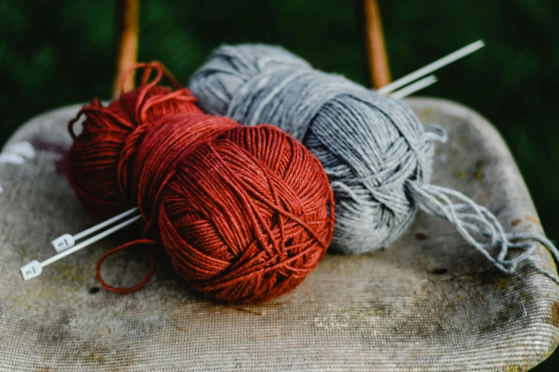 two balls of yarn sitting on top of a wooden chair, a portrait, unsplash, red brown and grey color scheme, gardening, stitching, knee