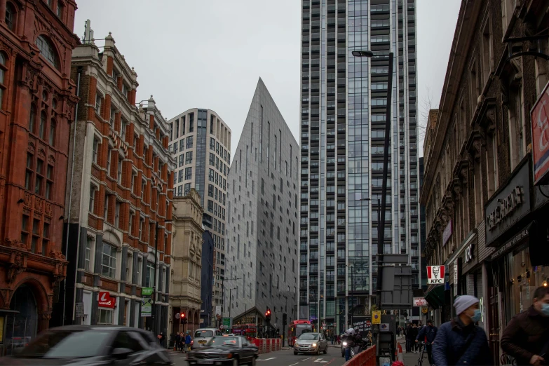 a group of people walking down a street next to tall buildings, a picture, london architecture, square, neo - gothic architecture, street corner