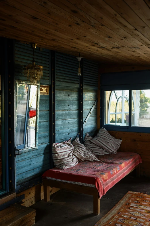 a bed sitting on top of a wooden floor next to a window, unsplash, maximalism, soviet bus stop, moroccan, barn, dark teal couch