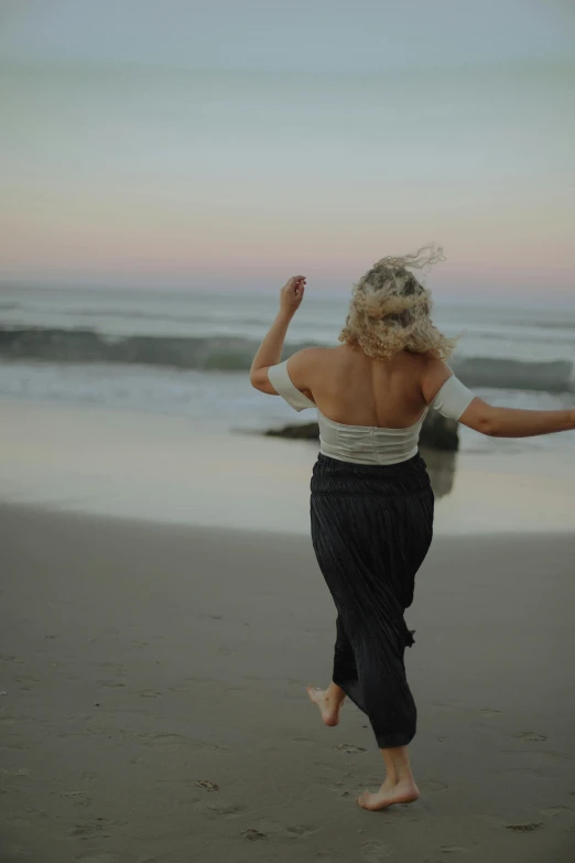 a woman standing on top of a beach next to the ocean, dancing on the beach, profile image