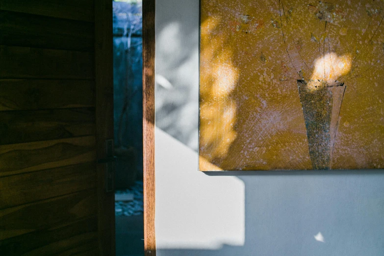 a vase sitting on top of a table next to a painting, inspired by Peter Zumthor, unsplash, light and space, door, dappled afternoon sunlight, ochre, a high angle shot