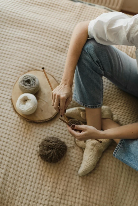 a woman sitting on top of a bed next to a ball of yarn, inspired by Sarah Lucas, trending on pexels, spinning hands and feet, with a wooden stuff, gardening, brown