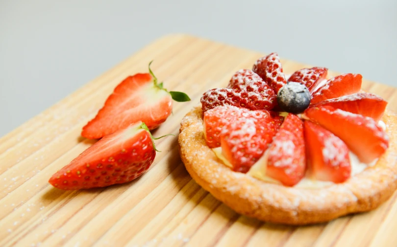 a wooden cutting board topped with a pastry covered in strawberries, by Matthias Stom, pexels, fan favorite, multicoloured, close - up photo, flan